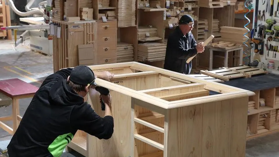 A craftsman assembling a wooden cabinet frame