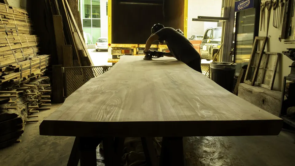 A craftsman sanding a long timber table top