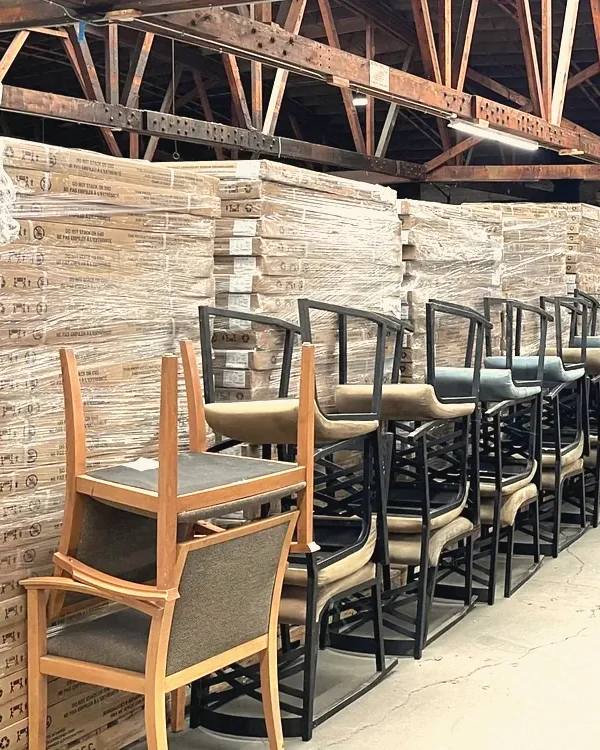 Rows of finished chairs and shrink-wrapped stacks of furniture in a large warehouse