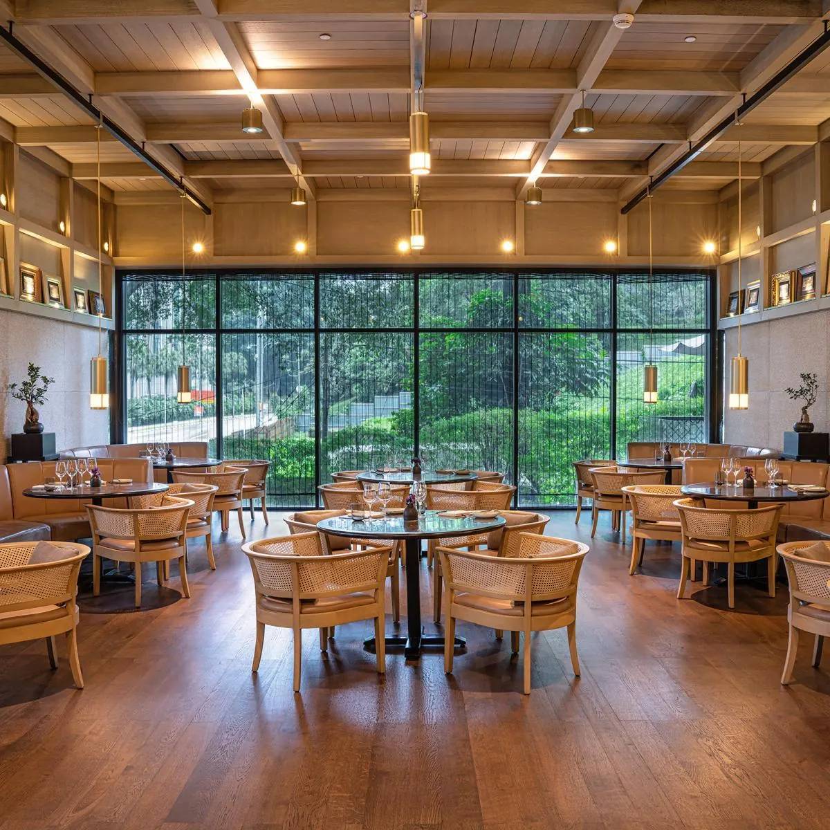 A restaurant hall with a coffered timber ceiling, round tables and cushioned wooden armchairs
